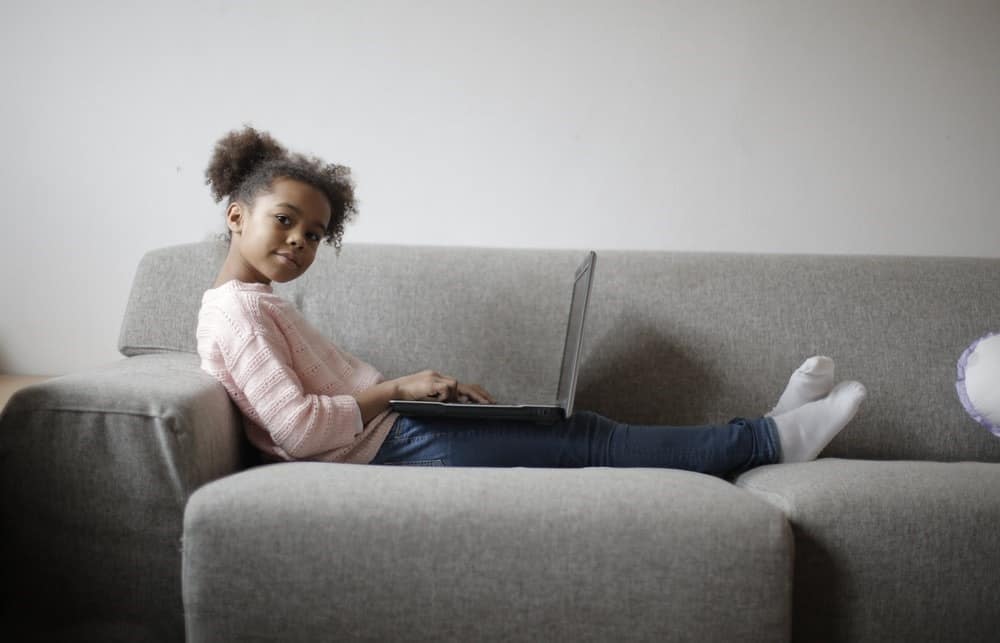 A young girl attending online classes while sitting on a couch at home