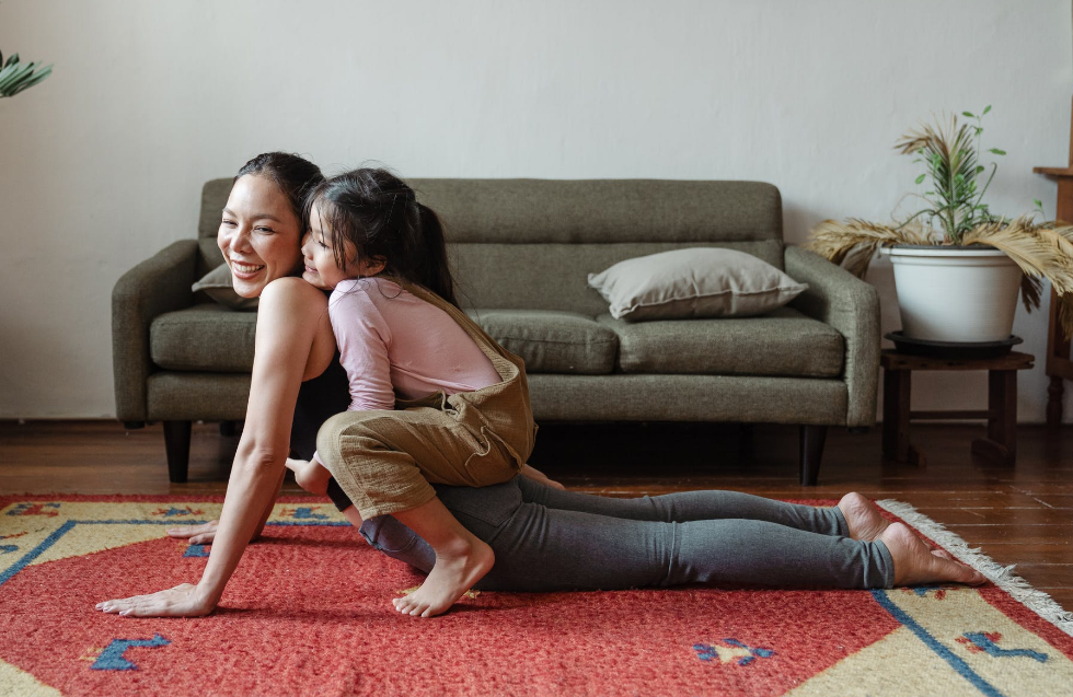 A girl is sitting on her mom as they do yoga