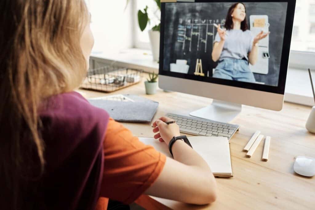 A girl takes notes as her teacher teaches her in an online class