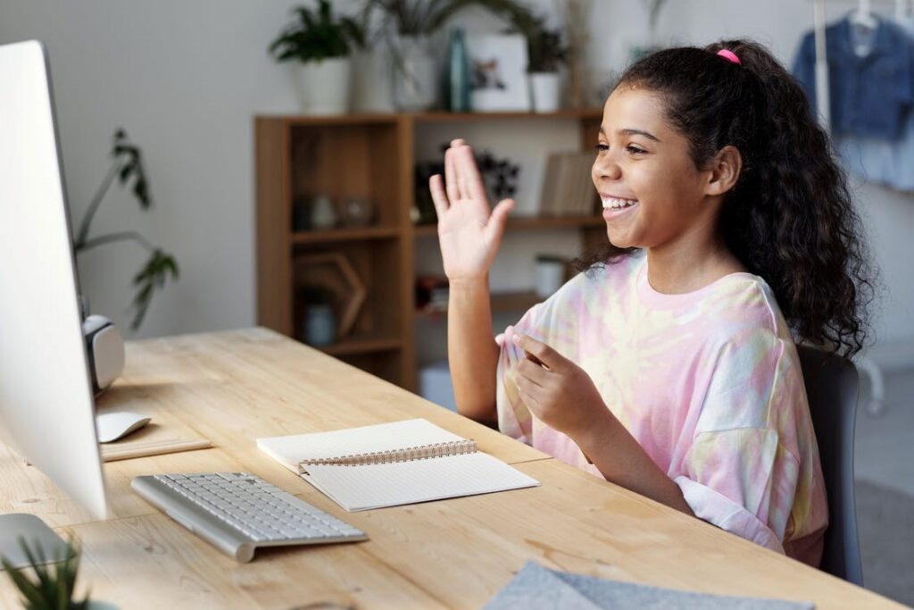 Chica feliz saludando en una pantalla durante una clase en línea.