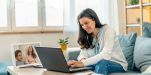 Expat mother smiling while choosing an online bilingual elementary school for her family on a laptop.