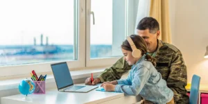 A father in military uniform helps his daughter with online school for military and expat families overseas.